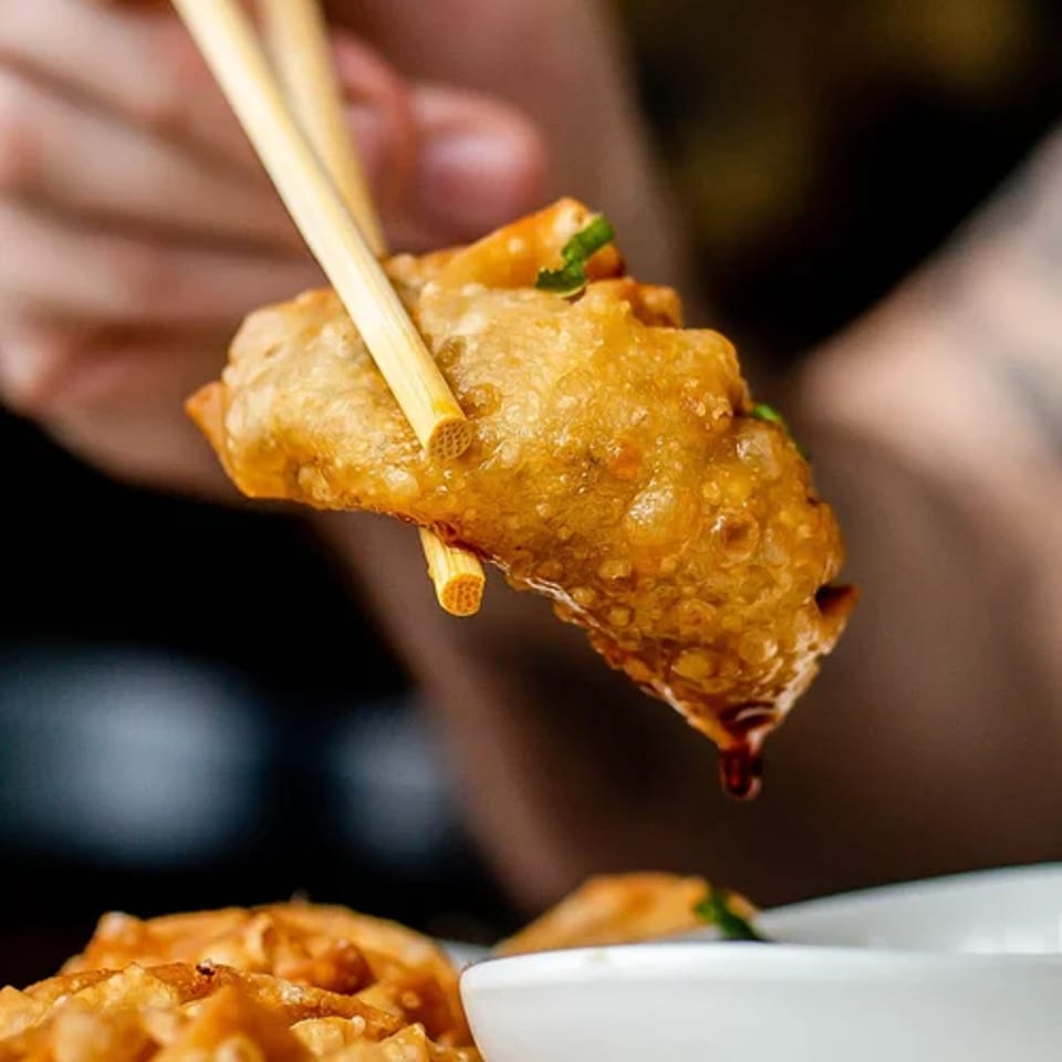Chopsticks lift a crispy wonton above a dipping bowl.