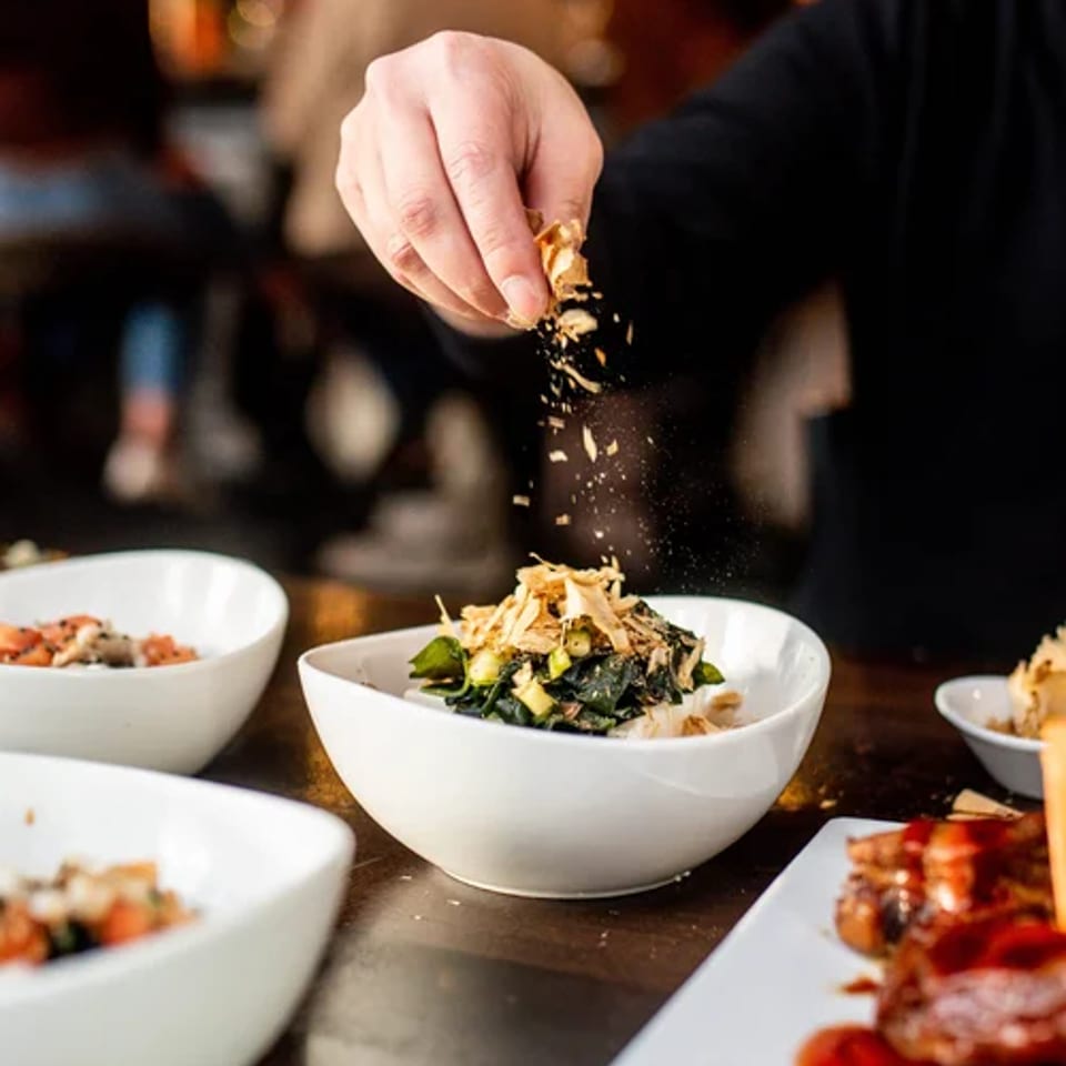 A chef adds garnish to a bowl at the kitchen counter.