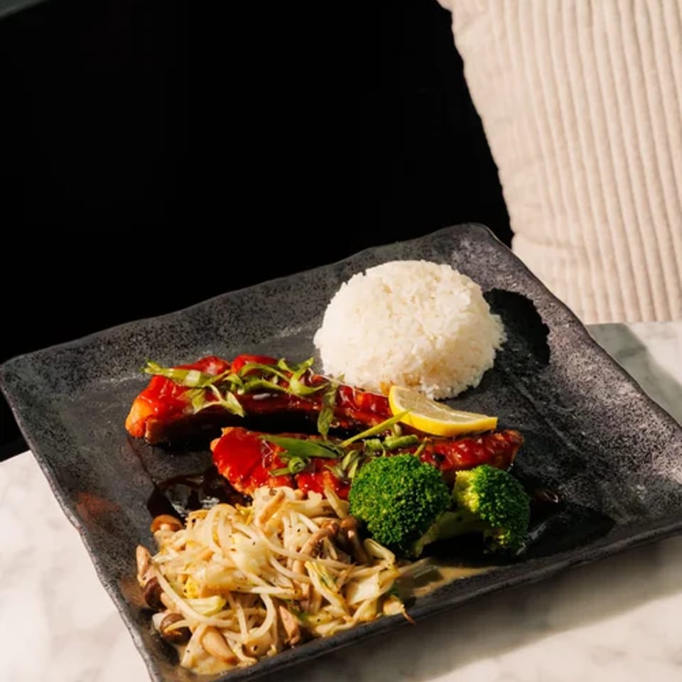 Salmon teriyaki served with rice, broccoli, and vegetables on a black plate.